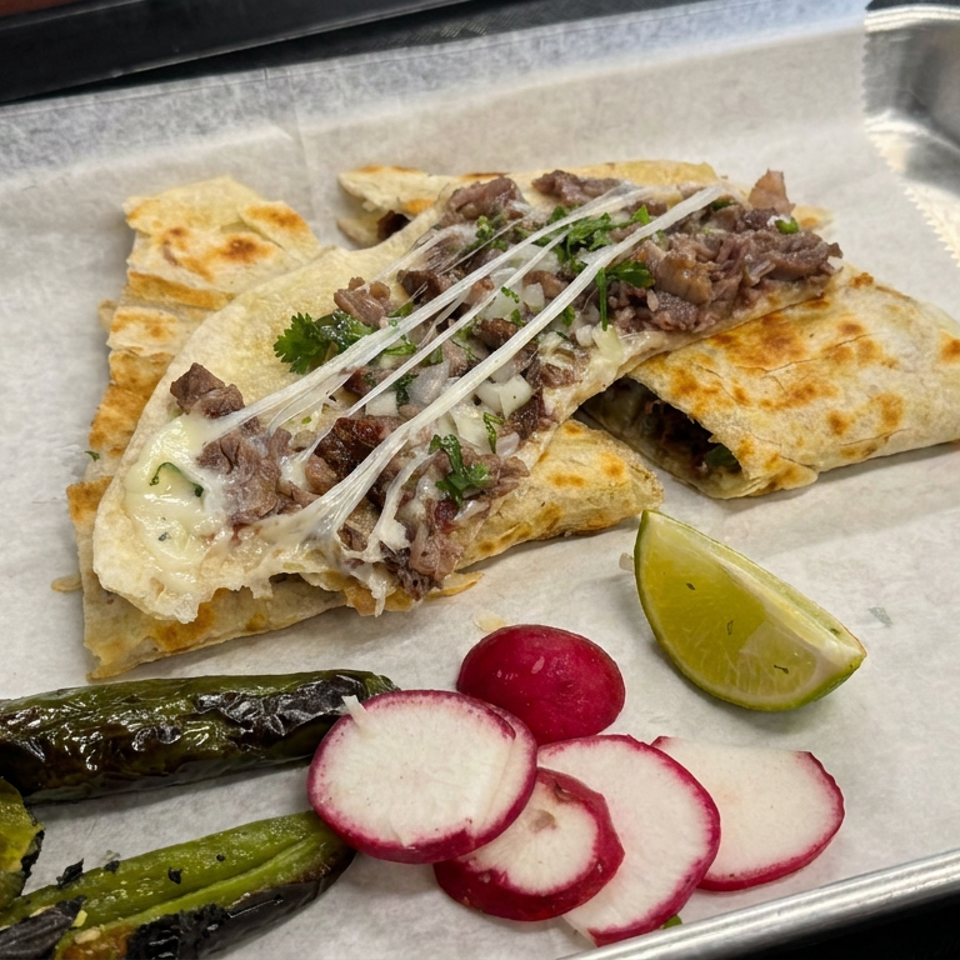 Steak quesadillas with melted cheese, cilantro, and onions served with grilled peppers, radishes, and a lime wedge on a metal tray.